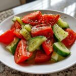 Nahaufnahme eines leuchtend roten Tomaten-Gurken-Salat mit viel frischem Dressing und Kräutern.