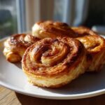 Nahaufnahme von fluffigen Apfel-Zimt-Roll-Ups aus Blätterteig auf einem weißen Teller.