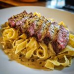 Teller mit Bandnudeln, belegt mit aufgeschnittenem Steak und übergossen mit grüner Pfeffersauce.