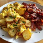 Teller mit klassischem Bauernfrühstück: goldbraun gebratene Kartoffelscheiben, fluffiges Rührei und knuspriger Speck.
