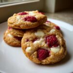 Nahaufnahme von gestapelten, saftigen Weiße-Schokolade-Himbeer-Cookies auf einem weißen Teller.