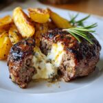 Aufgeschnittenes Bifteki mit Fetafüllung und Rosmarinkartoffeln auf einem Teller.