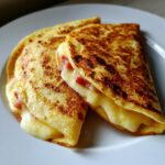 Zwei goldbraun gebratene Cheese-Wraps aus der Pfanne, gefüllt mit reichlich geschmolzenem Käse und Schinkenwürfeln.