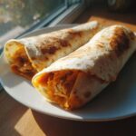 Zwei fertig gerollte und leicht angebratene Chicken-Cheese-Wraps gefüllt mit geschreddertem Hähnchen und Käse auf einem weißen Teller.