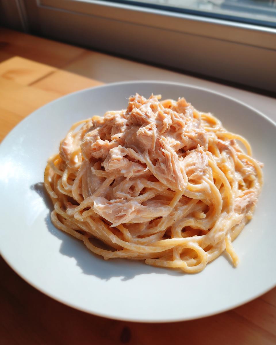 Nahaufnahme einer cremigen Portion Thunfisch-Frischkäse-Pasta mit viel Thunfisch obenauf, angerichtet auf einem weißen Teller.