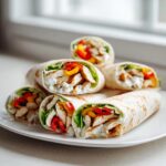 Stapel von saftigen Hähnchen-Wraps mit Joghurtsauce, Hähnchenstreifen, Paprika und Salat auf einem weißen Teller.