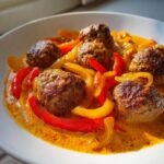 Frikadellen in Paprikarahm mit leuchtend roten und gelben Paprikastreifen in cremiger Sauce.