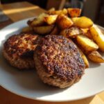 Zwei perfekt gebratene Frikadellen mit knusprigen Bratkartoffeln auf einem weißen Teller.