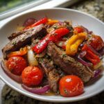 Nahaufnahme der Griechische Steakpfanne mit Kräutern, mit saftigen Steakstreifen, roten Zwiebeln, Paprika und Kirschtomaten.