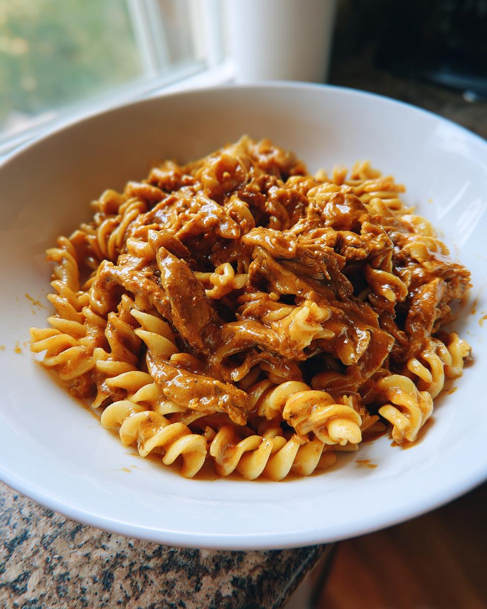 Nahaufnahme einer weißen Schüssel mit cremiger Gyros-Nudelpfanne in Metaxasauce und Spiralnudeln.