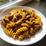 Nahaufnahme einer Portion Gyros-Nudelpfanne in cremiger Metaxasauce mit Spiralnudeln auf einem weißen Teller.