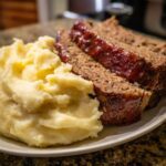 Zwei saftige Scheiben Hackbraten mit glänzender Glasur neben cremigem Kartoffelpüree auf einem Teller.