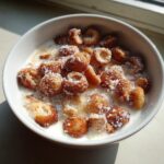 Nahaufnahme einer weißen Schüssel mit selbstgemachtem Mini-Donut-Cereal, bestreut mit Puderzucker und Milch.