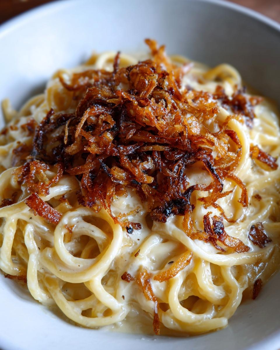 Nahaufnahme von Nudeln mit Sahne und einer großzügigen Portion knuspriger Röstzwiebeln.