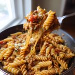 Nahaufnahme einer Gabel mit Nudelpfanne mit Hackfleisch und Schmand, wobei der geschmolzene Käse lange Fäden zieht.