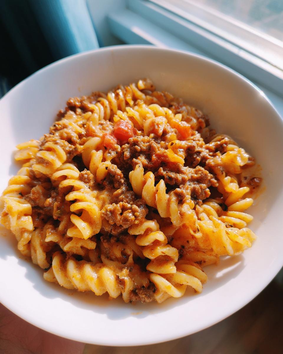 Eine Schüssel Nudelpfanne mit Hackfleisch und Schmand, leuchtend im Sonnenlicht neben einem Fenster.