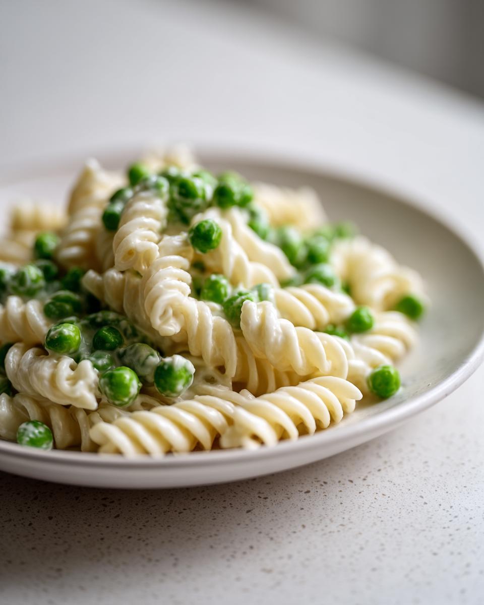 Nahaufnahme von cremigem Nudelsalat klassisch mit Erbsen und Spiralnudeln auf einem hellen Teller.