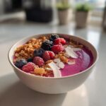 Nahaufnahme einer leuchtend pinken Pink-Dragonfruit-Smoothie-Bowl, garniert mit gefrorenen Beeren, Granola und Kokoschips.