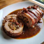 Anschnitt von saftigen Rinderrouladen Hausfrauenart umwickelt mit Speck und üppig bedeckt mit dunkler Soße.