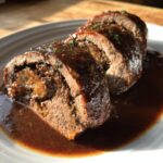 Anschnitt von saftigen Rinderrouladen in dunkler Bratensauce, reichhaltig gefüllt und glänzend.