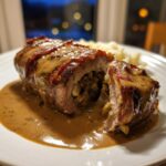 Anschnitt einer Rinderroulade mit Rahmsauce, gefüllt mit Zwiebeln, auf einem Teller.
