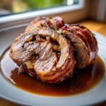 Zwei saftige Scheiben Rinderrouladen mit Speck-Zwiebel-Füllung in dunkler Soße.