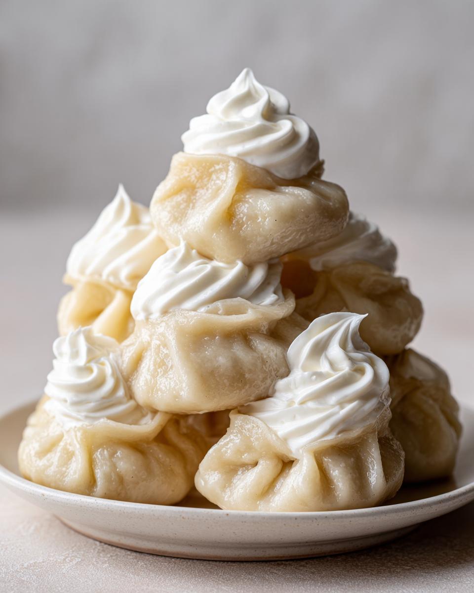 Ein Turm aus gekochten Russische Pelmeni mit Sauerrahm-Tupfen auf einem hellen Teller.