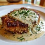 Nahaufnahme eines panierten Schnitzels, übergossen mit cremiger Knoblauchrahmsauce und Petersilie.