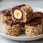 Ein aufgeschnittenes Stück Schoko-Bananen-Sushi zeigt die Bananenfüllung, umgeben von Reis und Schokoladenglasur.