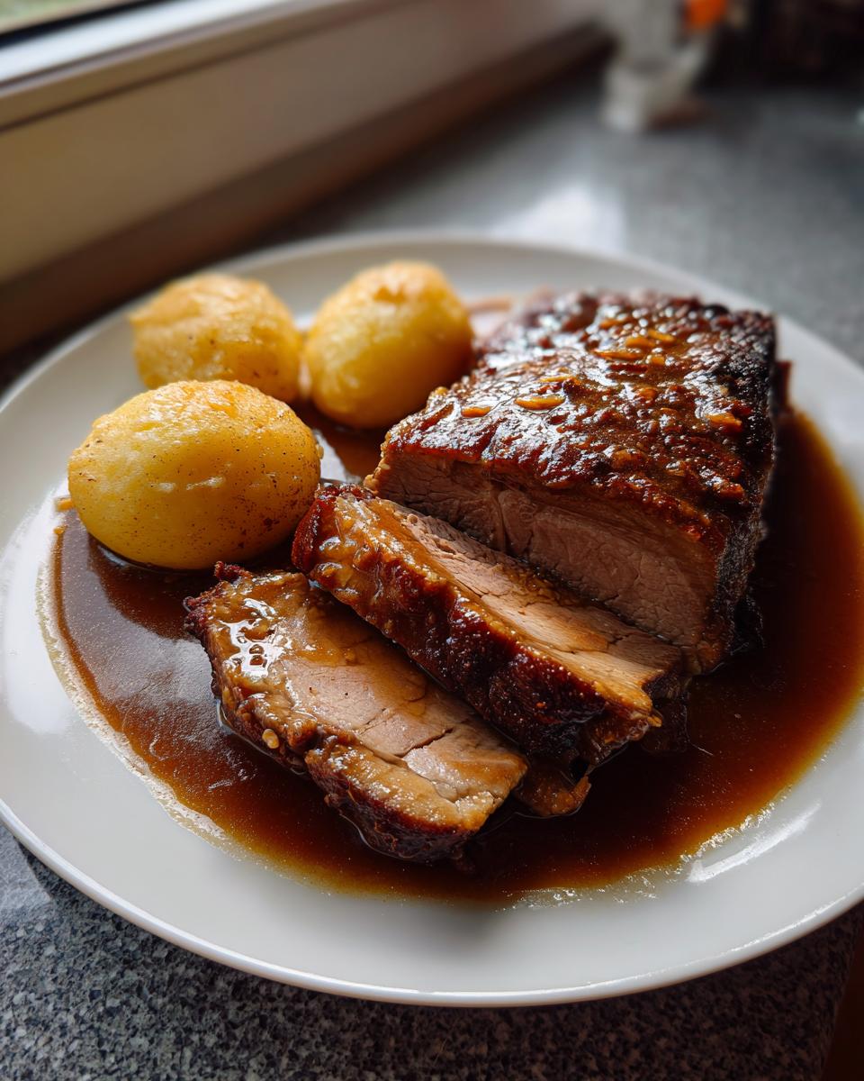 Teller mit aufgeschnittenem Schweinebraten mit Knödeln, übergossen mit dunkler Soße.