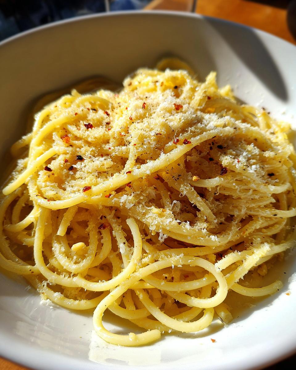Nahaufnahme von saftigen Spaghetti mit Knoblauchöl und reichlich geriebenem Parmesan und Chiliflocken.