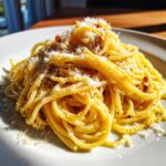 Nahaufnahme von saftigen Spaghetti mit Knoblauchöl und reichlich frisch geriebenem Parmesan.