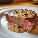 Ein perfekt gegartes Steak mit rosa Kern, übergossen mit cremiger Pfeffersauce voller ganzer Pfefferkörner.