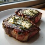 Zwei saftige Steaks mit schmelzender Rosmarin-Knoblauch-Butter auf einem weißen Teller.