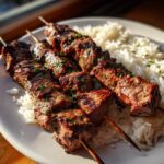 Drei saftige Spieße mit gegrilltem Steak-Souvlaki auf einem Bett aus weißem Reis.