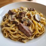 Teller mit cremigen Tagliatelle mit Steakstreifen und Pilzrahm, reichhaltig garniert.