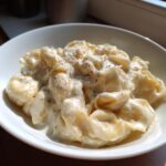 Nahaufnahme von Tortellini in einfacher Sahnesauce, bestreut mit frisch gemahlenem Pfeffer in einer weißen Schüssel.