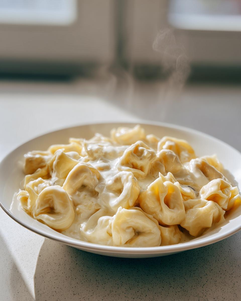 Nahaufnahme von dampfenden Tortellini in einfacher Sahnesauce in einem weißen Teller.