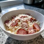 Nahaufnahme von Wurstsalat schwäbische Art mit Wurstscheiben, Zwiebeln und viel geriebenem Käse in einer weißen Schüssel.