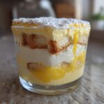 Nahaufnahme eines geschichteten Zitronen-Tiramisu im Glas mit Löffelbiskuits und Puderzucker.
