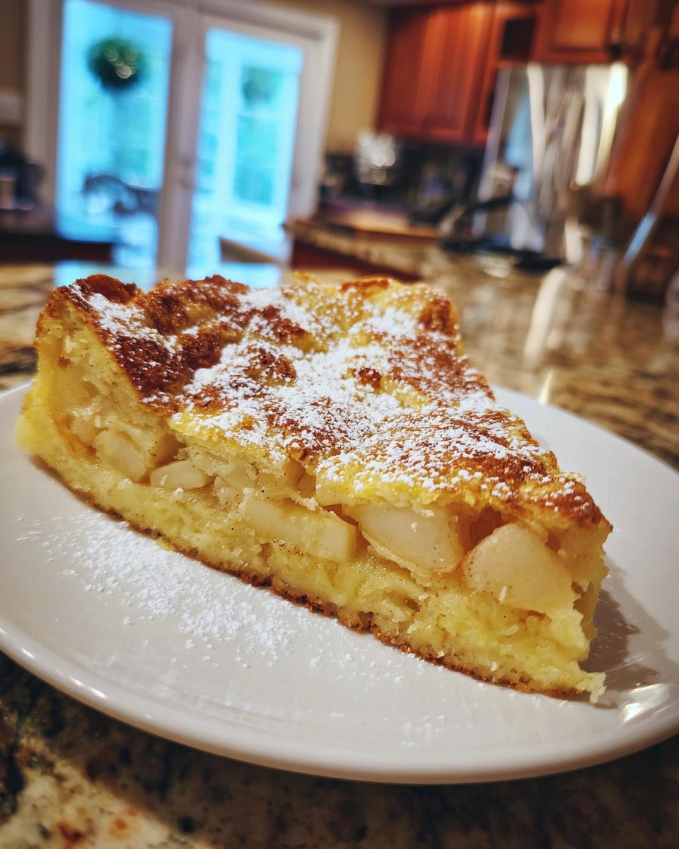 Ein dickes Stück Apfelpfannkuchen aus dem Ofen, bestäubt mit Puderzucker, auf einem weißen Teller.