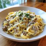 Teller mit cremigen Bandnudeln mit Hackfleisch in Parmesan-Sahne, bestreut mit geriebenem Käse und Petersilie.