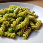 Nahaufnahme von leuchtend grüner Cremige Erbsen-Pasta mit ganzen Erbsen, vermischt mit Spiralnudeln auf einem weißen Teller.