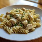 Nahaufnahme von cremigen One-Pot-Hähnchen-Nudeln mit saftigen Hähnchenstücken und grünen Erbsen auf einem weißen Teller.