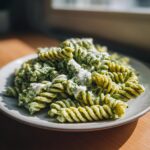 Nahaufnahme von Cremige Pesto-Frischkäse-Nudeln (Fusilli) mit cremiger Soße auf einem grauen Teller.