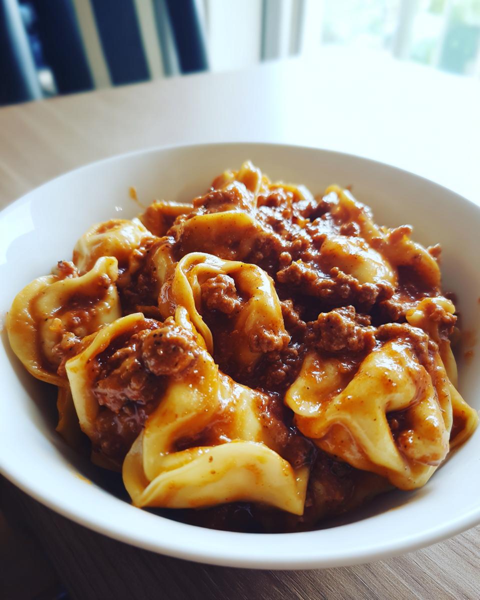 Eine weiße Schüssel gefüllt mit saftigen Tortellini, übergossen mit einer reichhaltigen, cremigen Hackfleischsauce.