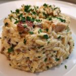 Nahaufnahme von cremigem Hähnchen-Frischkäse-Orzo, garniert mit Petersilie auf einem weißen Teller.