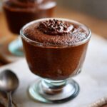 Nahaufnahme eines cremigen Schoko-Grießdessert in einem Glas, garniert mit Schokostreuseln.