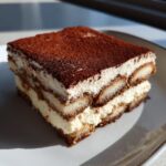 Ein saftiges Stück Einfaches Tiramisu ohne Ei mit Schichten aus Creme und Löffelbiskuits, bestäubt mit Kakao.