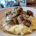 Teller mit saftigen Frikadellen in Rahmsauce und cremigem Kartoffelpüree, garniert mit Petersilie.